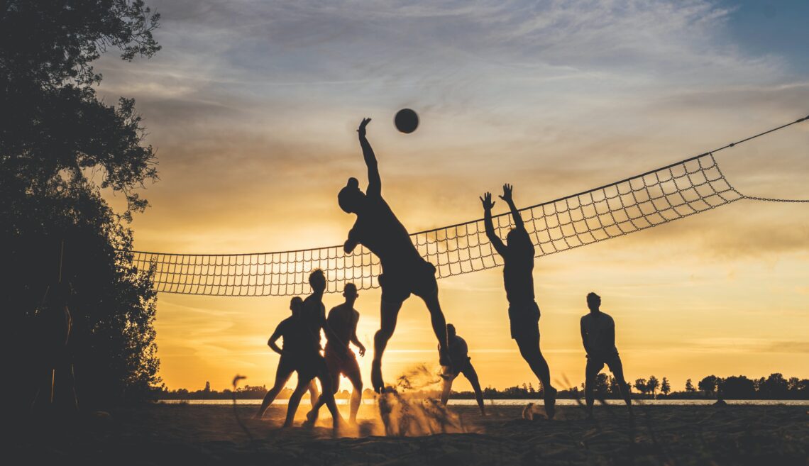a team playing voleyball outside with sunset behind
