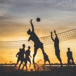 a team playing voleyball outside with sunset behind